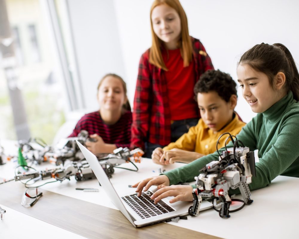 Group of happy kids programming electric toys and robots at robotics classroom